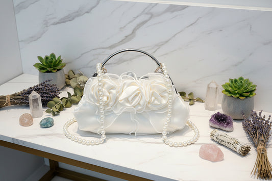 White handbag with floral design and pearl strap on a gray surface