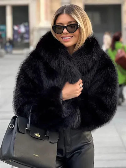 Woman wearing a black fur coat and sunglasses, holding a black handbag on a city street.