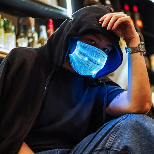Person wearing a dark hoodie and glowing blue face mask in a bar setting