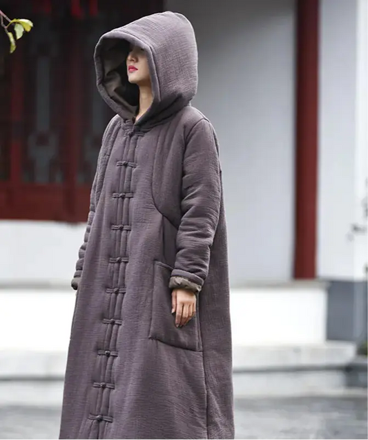 Person wearing a long, dark gray coat with a hood in an outdoor setting.