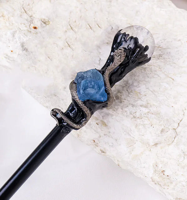 Decorative white crystal magic wand with black base, blue stone, and clear crystal on a marble background