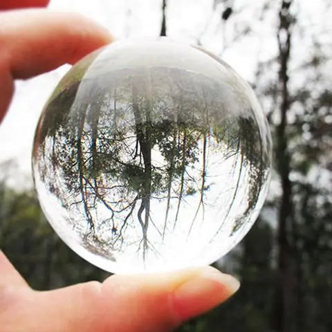 Clear crystal ball held by a hand with a forest reflection