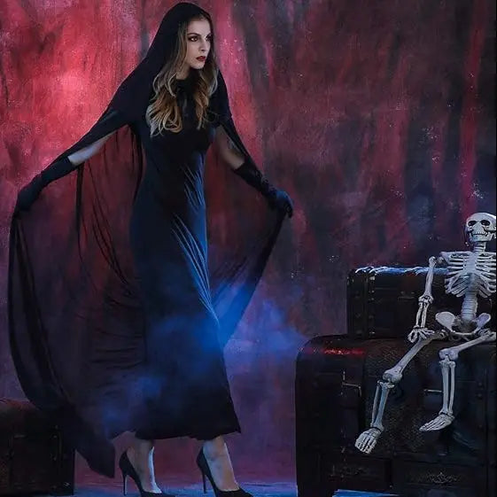 Woman in a black dress with a hood standing next to a skeleton against a dark background