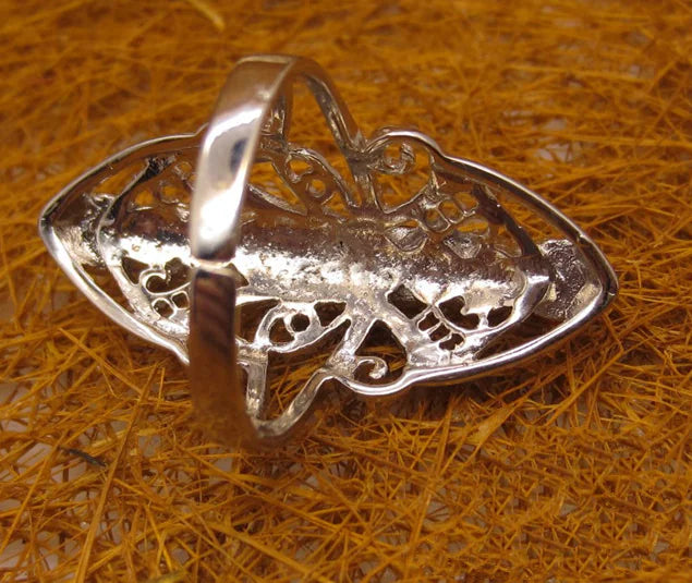 Silver pendant with intricate design on a textured orange surface