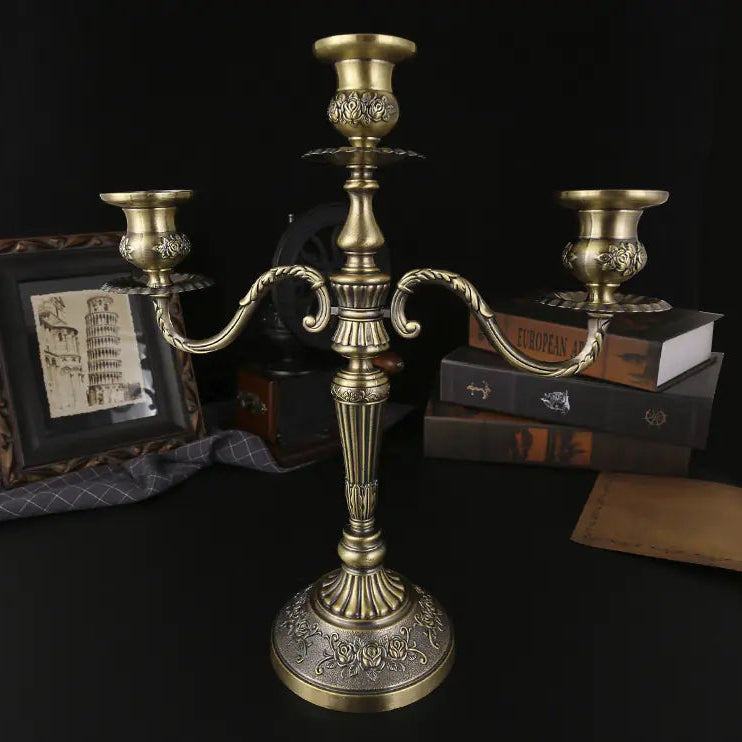 Bronze candelabrum on a dark surface with books and a picture frame in the background