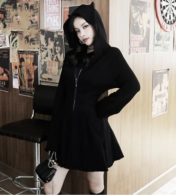 Person wearing a black hoodie and skirt in a room with posters on the wall.