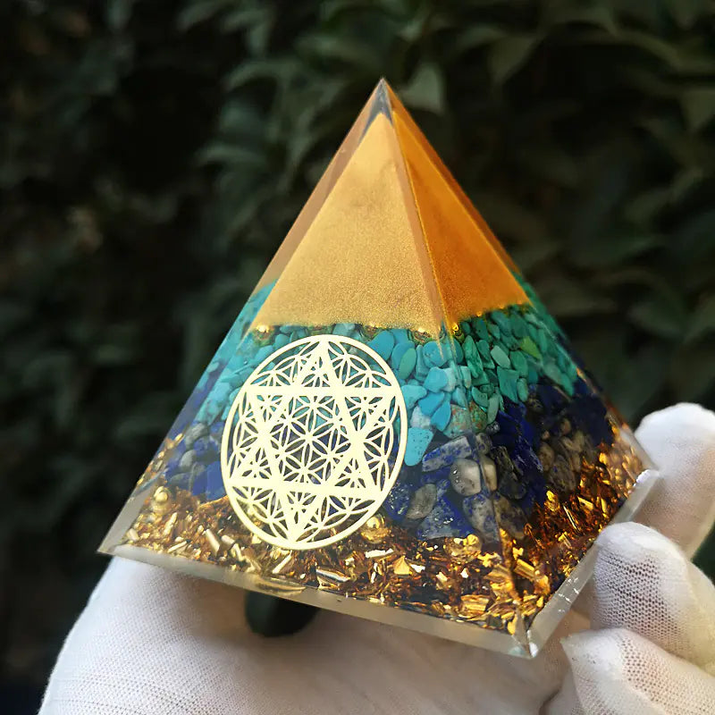 Pyramid-shaped crystal with geometric design held by a gloved hand against a dark background