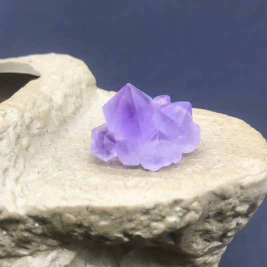 Purple crystal on a textured stone surface with a dark blue background