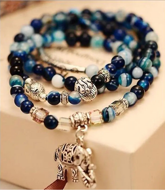 Set of blue and gold beaded bracelets with elephant charms on a beige surface