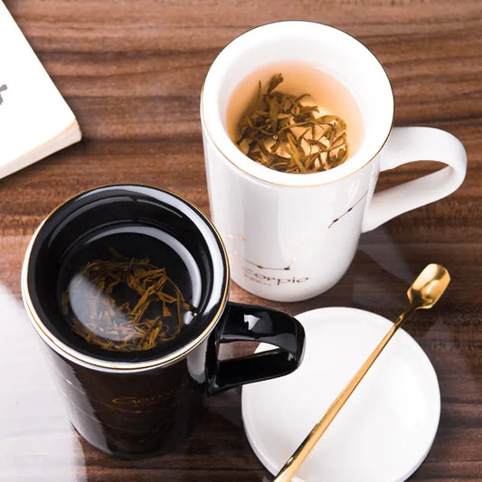 Two mugs with tea on a wooden table, one black and one white, with a spoon and book in the background.