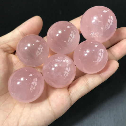Hand holding six pink crystal balls against a dark background