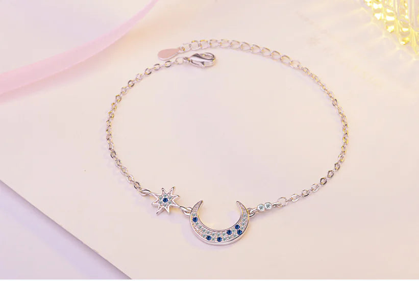 Silver bracelet with star and moon design on a light pink background