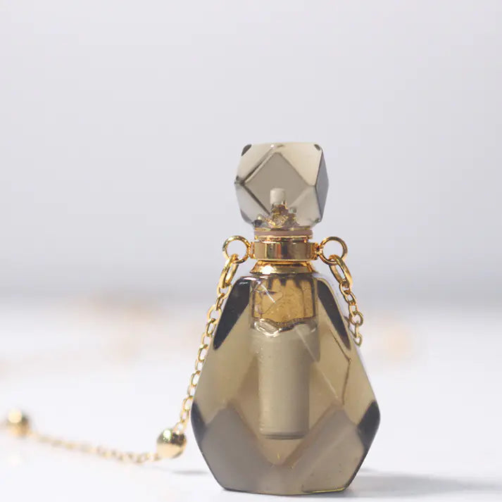 Gold and crystal perfume bottle with chain on a light gray background