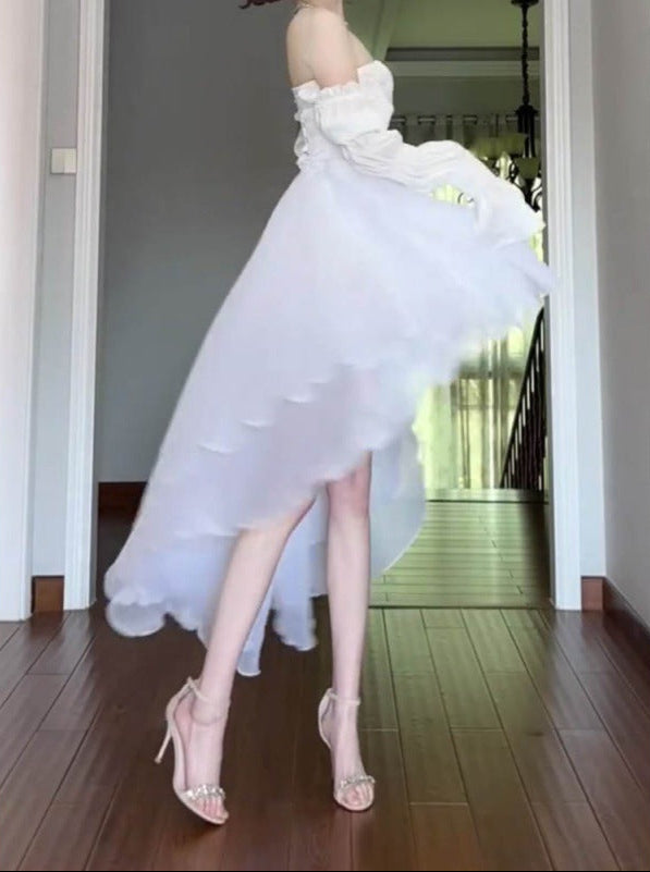 Woman wearing a white dress with ruffled top and high-low hem in a room.