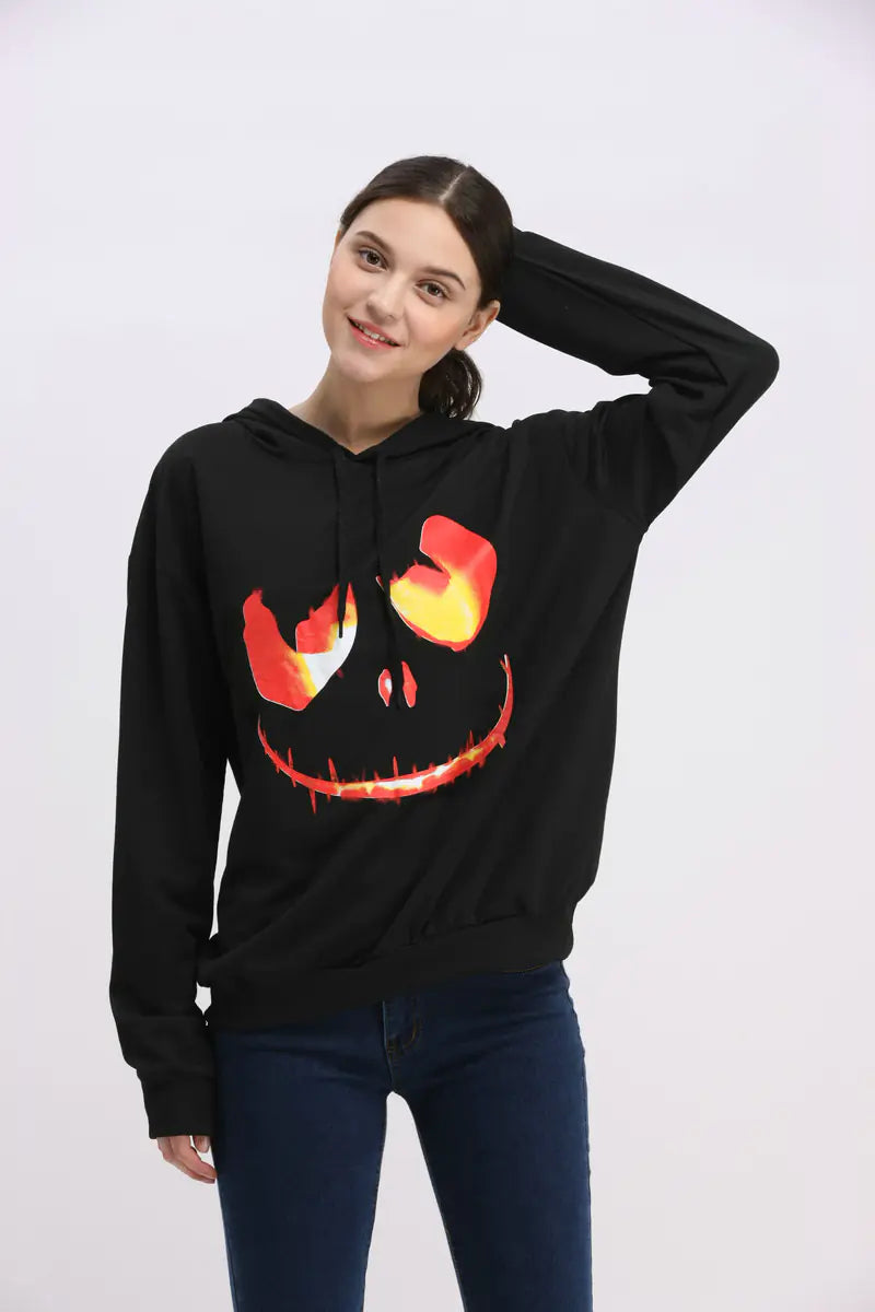 Person wearing a black hoodie with a jack-o'-lantern face design on a white background