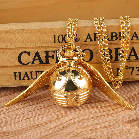 Gold necklace with a round pendant and wing-like extensions on a wooden surface.