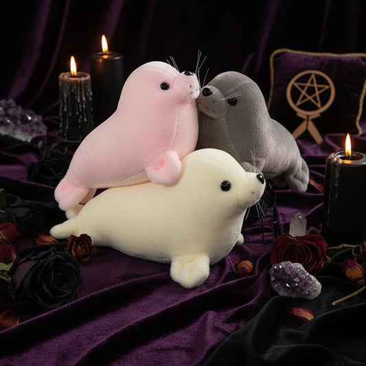 Three plush seal toys in pink, gray, and white on a textured surface with a blurred background.