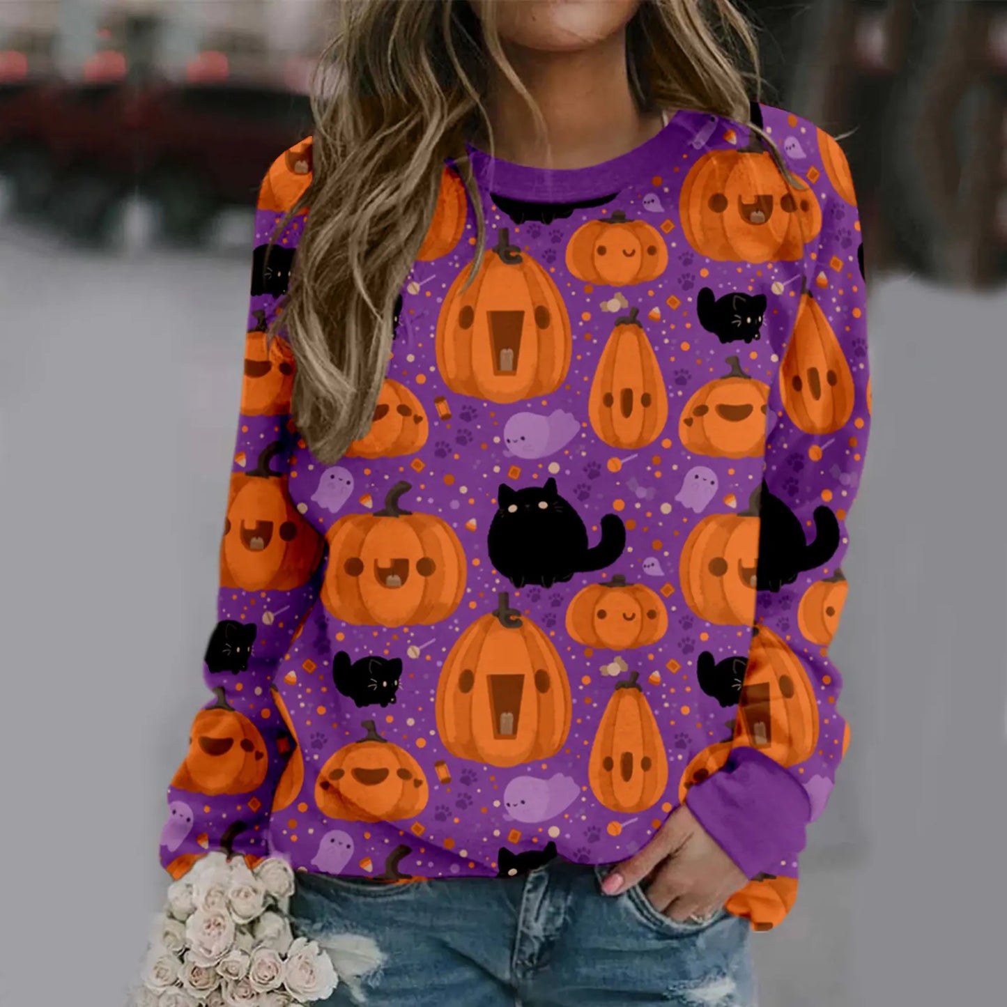 Person wearing a Halloween-themed purple sweatshirt with pumpkins and cats.