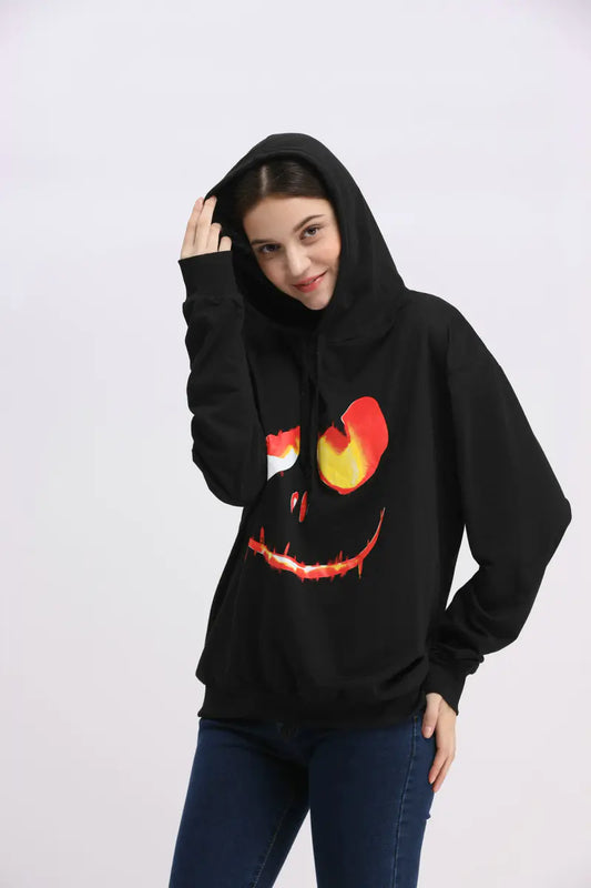 Person wearing a black hoodie with a jack-o'-lantern face design on a white background