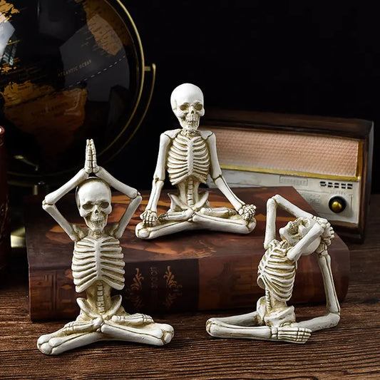 Three skeleton figurines in yoga poses on a wooden surface with a radio in the background.