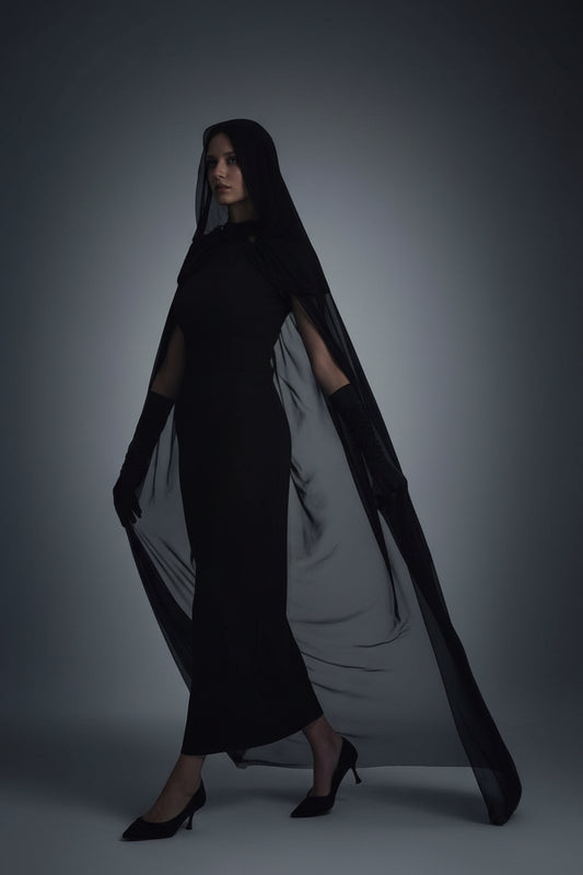 Woman wearing a long black and white lace cloak dress on a white background