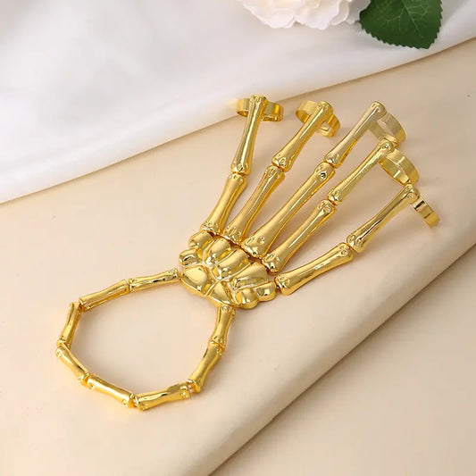 Gold skeleton hand with a ring on a beige surface with a white flower in the background