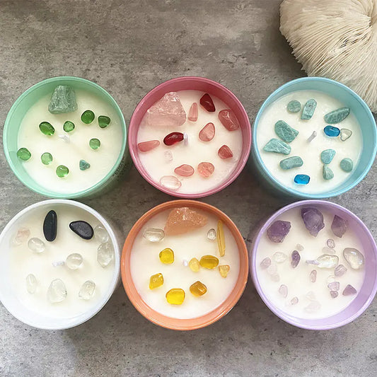 Set of six small candles in colorful containers with decorative stones on a gray surface.