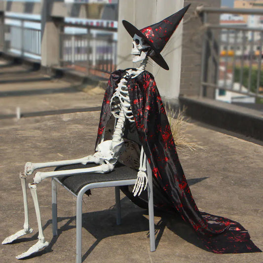 Skeletal figure in a witch costume with a black and red cape sitting on a chair outdoors.