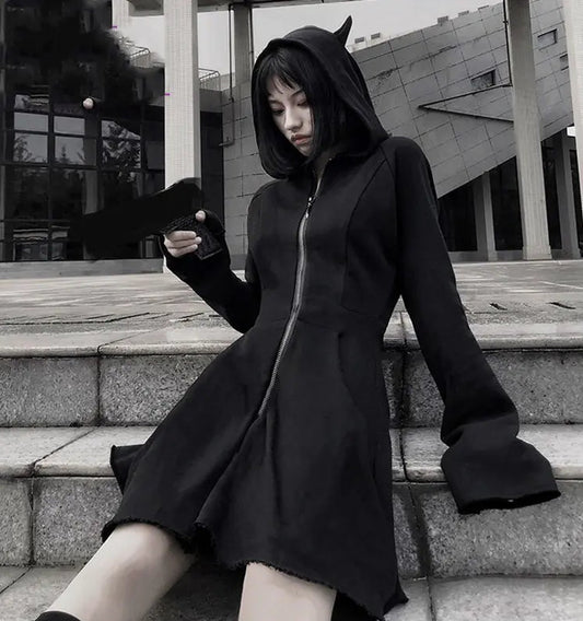 Person wearing a black hooded coat with devil horns sitting on steps outdoors.