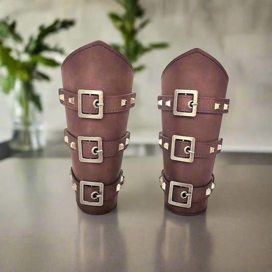 Pair of brown leather arm guards with gold buckles on a white background