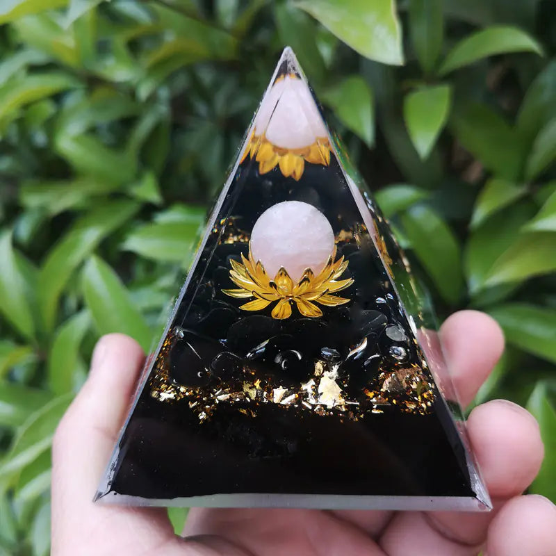 Triangular crystal pyramid with gold lotus designs held by a hand against a green leafy background