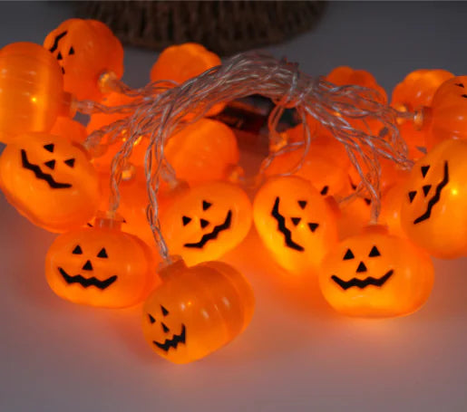 String of orange pumpkin lights with jack-o'-lantern faces on a white background