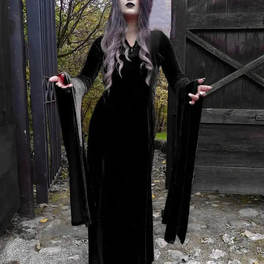 witch in a long black coat and dress standing in front of a wooden gate.