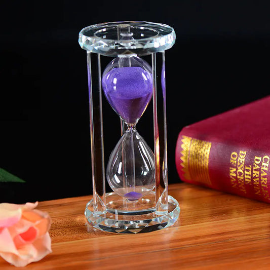 Sand timer with purple sand on a wooden surface next to a book