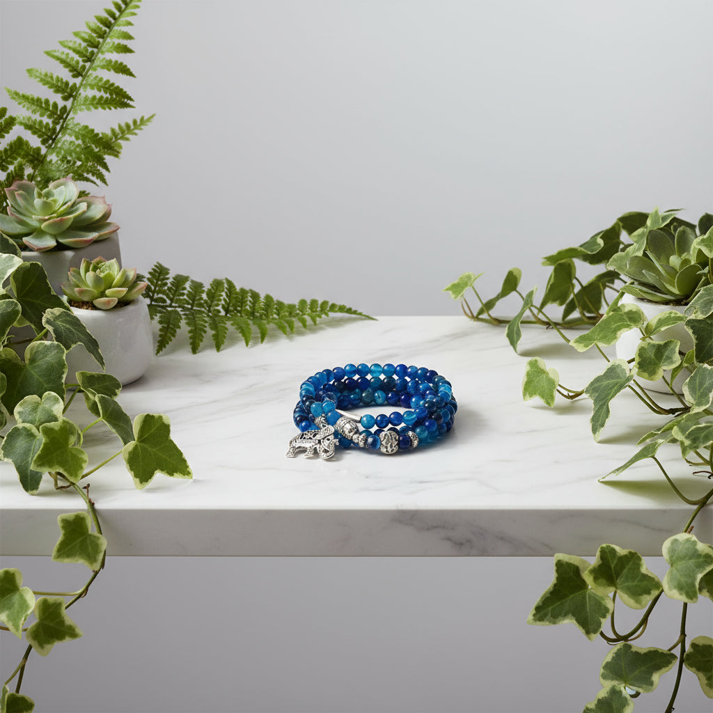 Blue beaded bracelet with silver elephant charms on a white fabric background