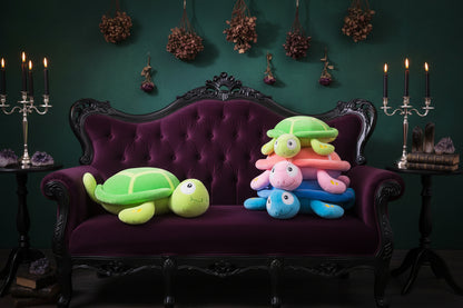 Stack of colorful turtle-shaped toys on a table with a large green turtle plush toy on a chair.