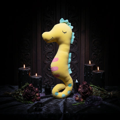 Yellow plush seahorse toy with green and pink accents on a beige background