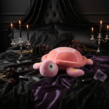 Pink plush turtle toy on a checkered tablecloth with a blurred indoor background