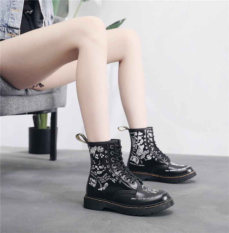 Black boots with white text and designs worn by a person sitting on a chair.