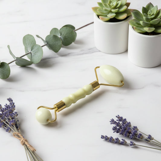 White facial roller with gold accents on a gray background