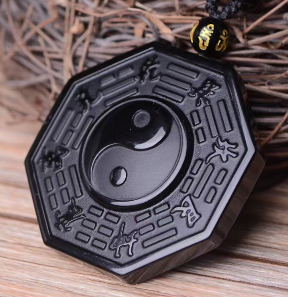 Black octagonal obsidian pendant with central yin yang circular design on a wooden surface