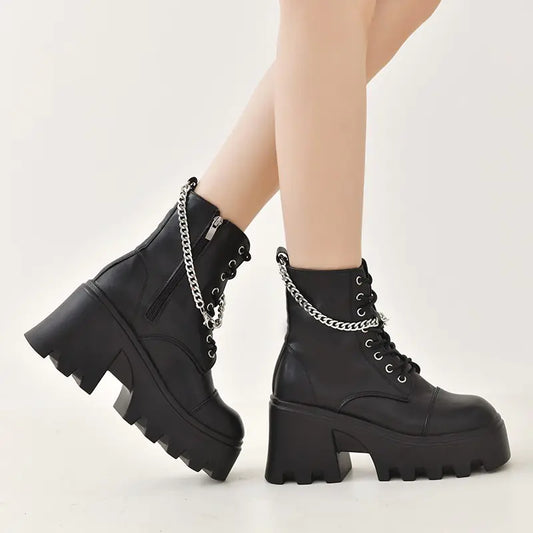 Black platform boots with chain details worn by a person on a white background