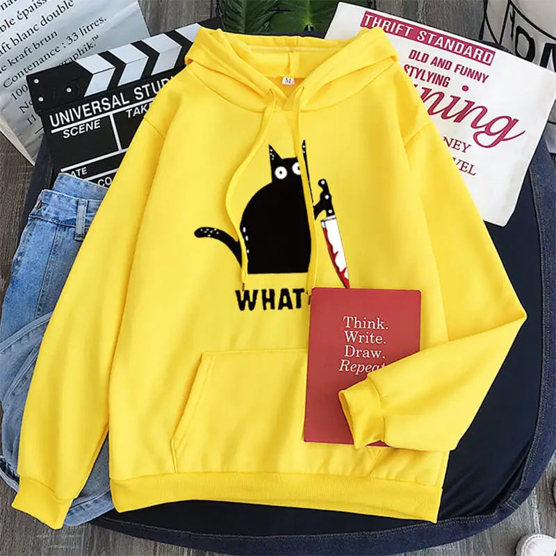 Yellow hoodie with a black cat graphic and text, placed on a surface with jeans and a book.