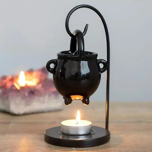 Black cauldron-shaped oil burner with a lit candle on a wooden surface.