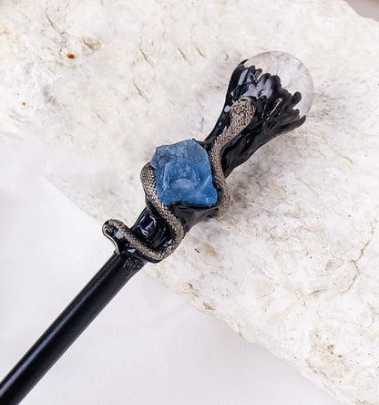 Decorative white crystal magic wand with black base, blue stone, and clear crystal on a marble background