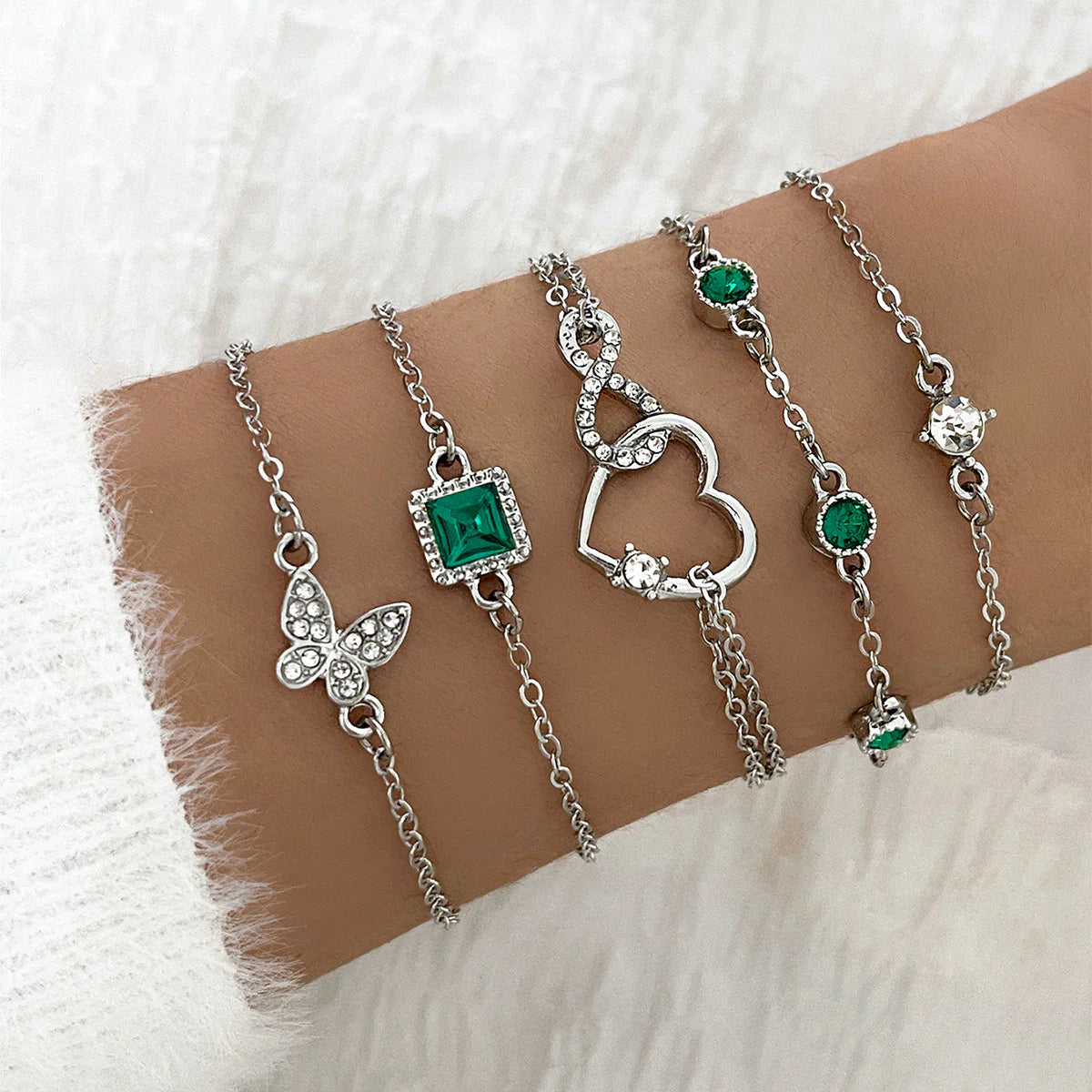 Silver bracelets with green gemstones on a wrist against a white background
