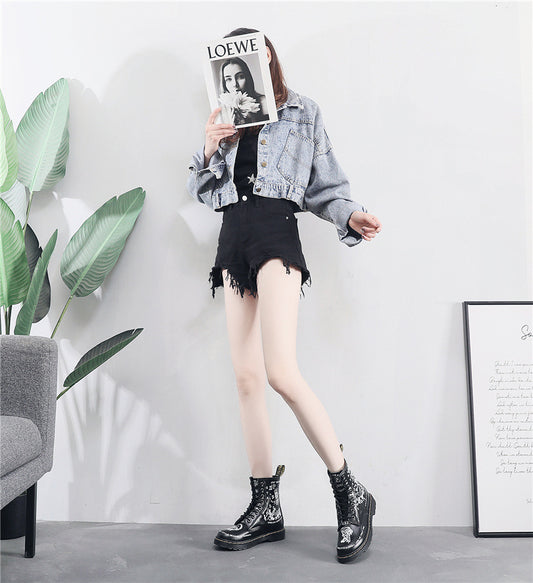 Person wearing a denim jacket, black skirt, and black boots in a room with a plant and framed picture.