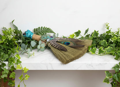 Decorative broom with peacock feathers and turquoise accents on a white background