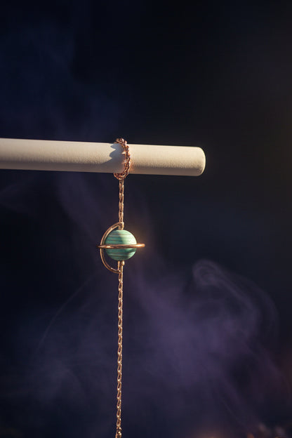 Bracelet with a turquoise bead and rose gold chain on a white surface.