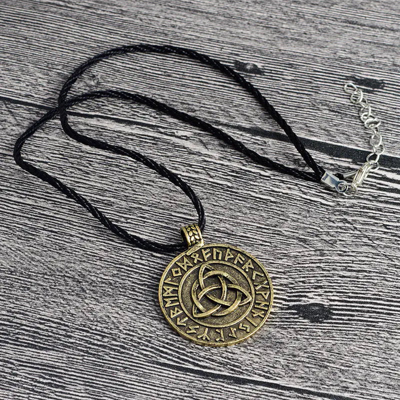 Bronze pendant necklace with intricate design on a black cord, placed on a wooden surface.